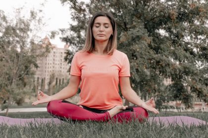 Adult woman practicing meditation on a yoga mat outdoors in a tranquil park setting.