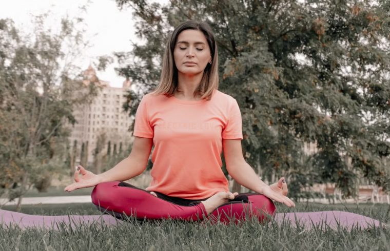 Adult woman practicing meditation on a yoga mat outdoors in a tranquil park setting.
