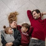 Smiling family of four lying on a blanket, sharing happiness and love indoors.