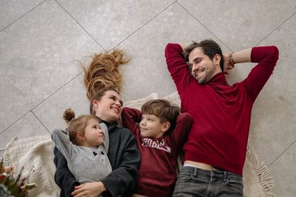 Smiling family of four lying on a blanket, sharing happiness and love indoors.