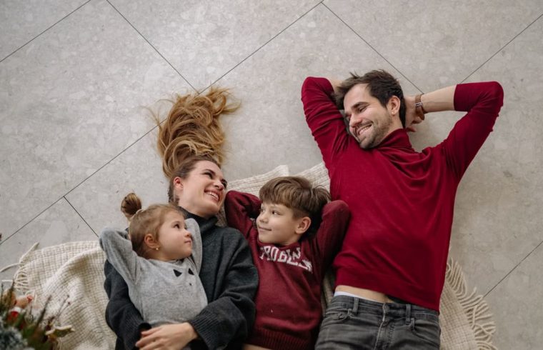 Smiling family of four lying on a blanket, sharing happiness and love indoors.