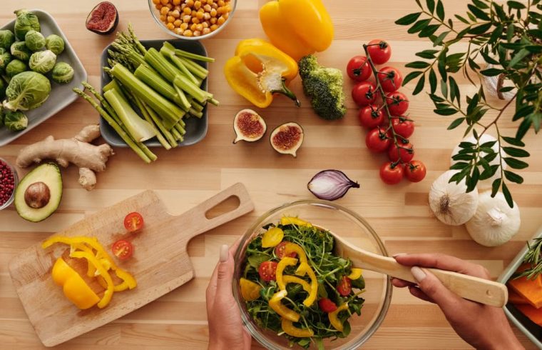 Top view of fresh vegetables and salad preparation on a wooden table, perfect for healthy eating concepts.